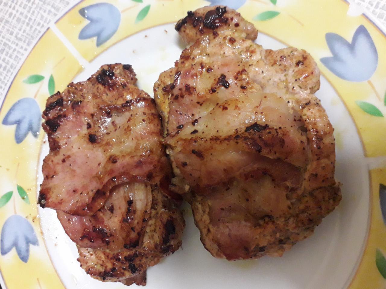 Dwa kawałki grillowanego mięsa na talerzu z żółto-białym wzorem kwiatowym, widoczne przypalone przyprawy i tłuszcz.