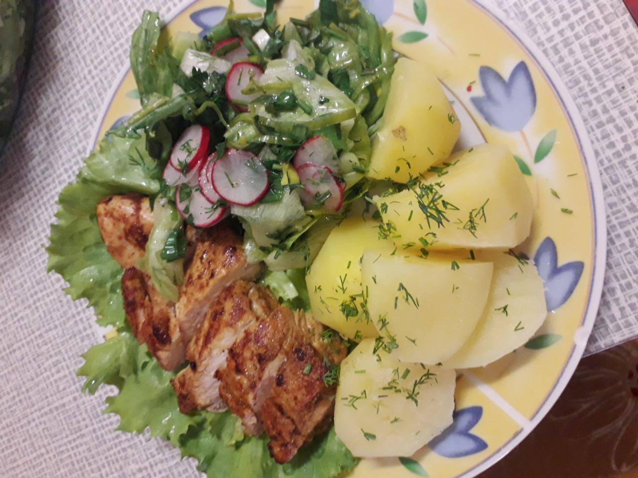 Żółty talerz z motywem kwiatowym, na którym znajduje się grillowany kurczak na liściach sałaty, sałatka z rzodkiewką i gotowane ziemniaki posypane koperkiem.