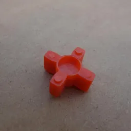 Pomarańczowe, plastikowe sprzęgło krzyżowe na tle płyty wiórowej.