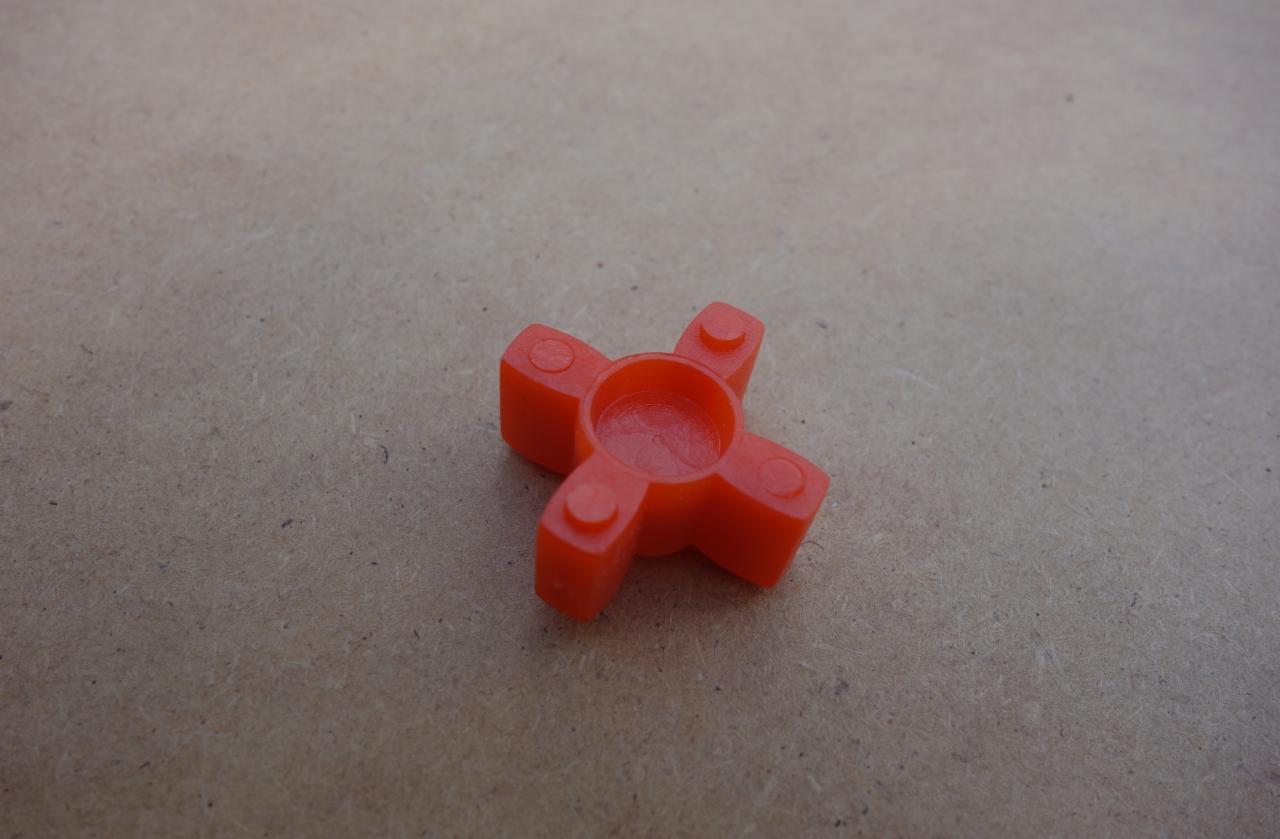 Pomarańczowe, plastikowe sprzęgło krzyżowe na tle płyty wiórowej.