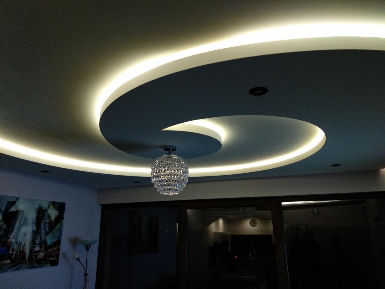 Podwieszany sufit w kształcie spirali z oświetleniem LED i kryształowym żyrandolem w nowoczesnym salonie.