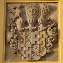 Renowacja - Kamienny herb z orłem i szachownicą na żółtej ścianie, detal architektoniczny w zabytkowym budynku.