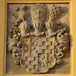 Kamienny herb z orłem i szachownicą na żółtej ścianie, detal architektoniczny w zabytkowym budynku.