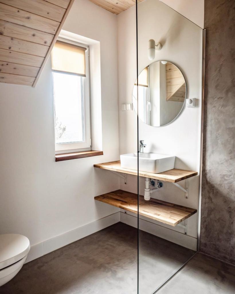 Minimalistyczna łazienka w skandynawskim stylu z szarą posadzką, drewnianym sufitem i umywalką na drewnianych półkach.