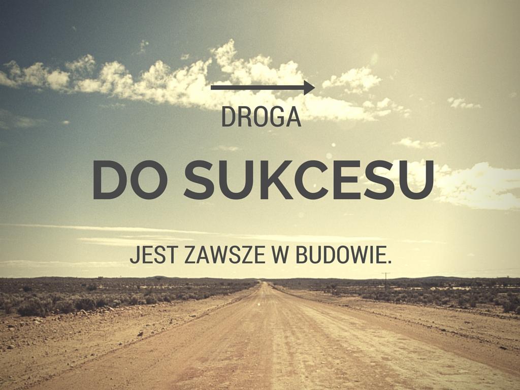 Długa, prosta droga przez pustynny krajobraz pod błękitnym niebem z chmurami, z tekstem 'DROGA DO SUKCESU JEST ZAWSZE W BUDOWIE' i strzałką w prawą stronę, symbolizująca ciągły rozwój...
