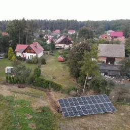 Montaż paneli słonecznych na gruncie w wiejskim otoczeniu, widok z góry na instalatorów pracujących przy panelach.