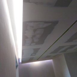 FACH-BUD Rafał Bobek - Sufit z płyt kartonowo-gipsowych w trakcie szpachlowania, widoczna zielona linia lasera wyznaczająca poziom, oświetlenie LED wzdłuż krawędzi.