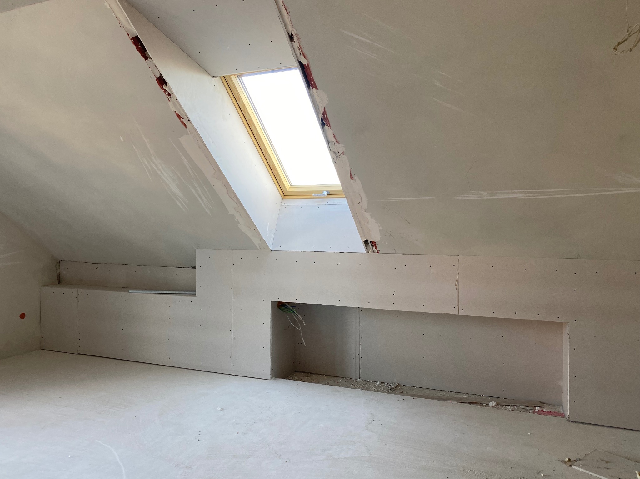 Montaż płyty karton gips na poddaszu w Damienicach, widoczne okno dachowe i przygotowane wnęki w ścianie.