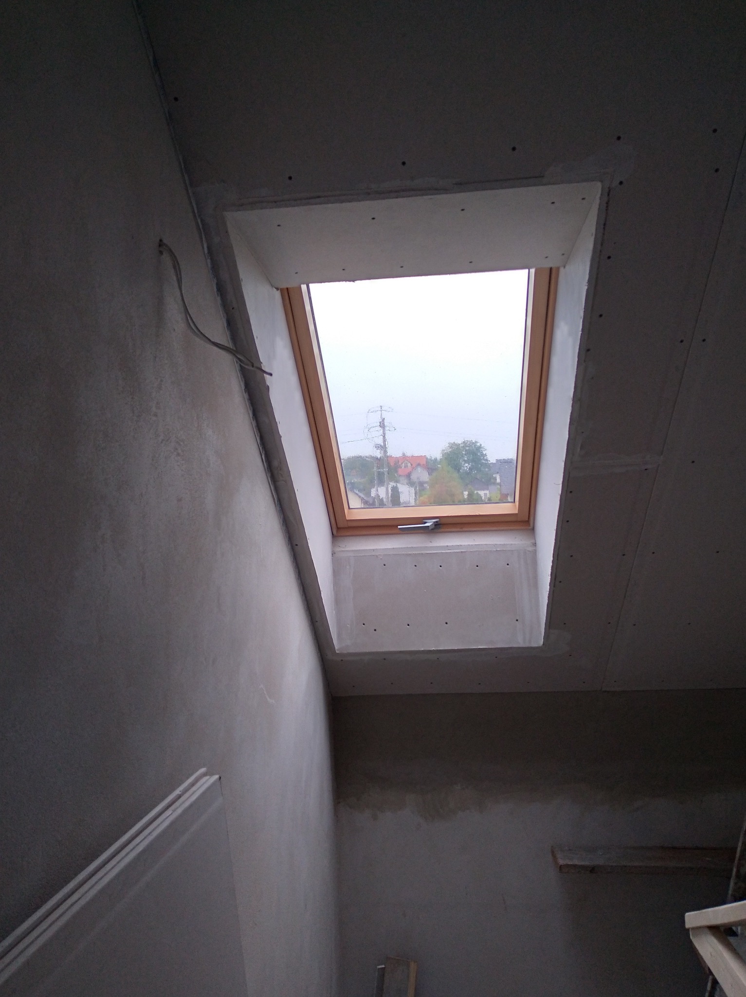 Wnętrze poddasza z oknem dachowym w trakcie montażu, widoczne płyty karton gips, szpachlowane łączenia i fragment ściany po szpachlowaniu.