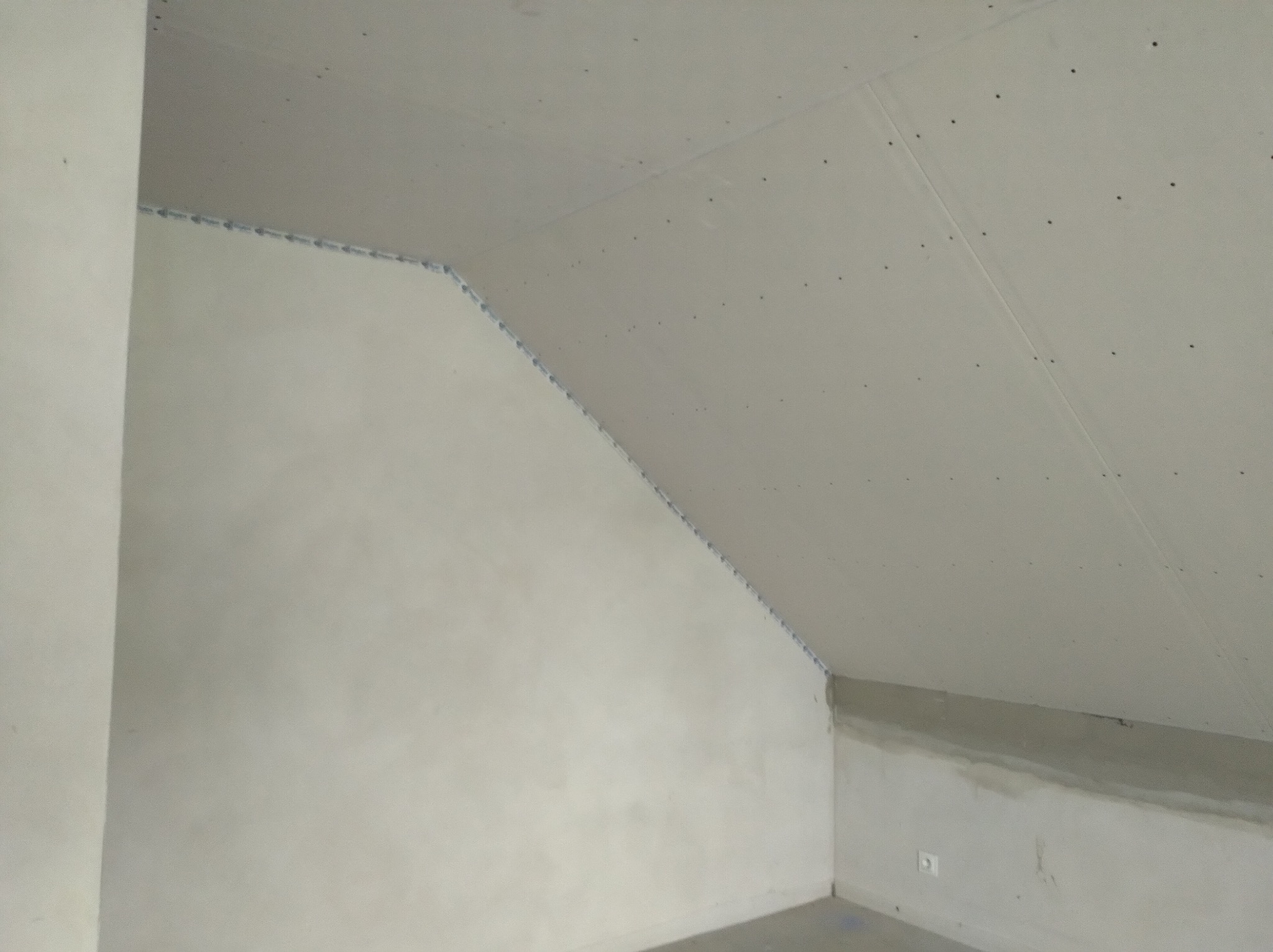 Poddasze w trakcie wykańczania: ściana skośna z zamontowaną płytą kartonowo-gipsową, widoczne łączenia płyt zabezpieczone taśmą, oczekujące na szpachlowanie.