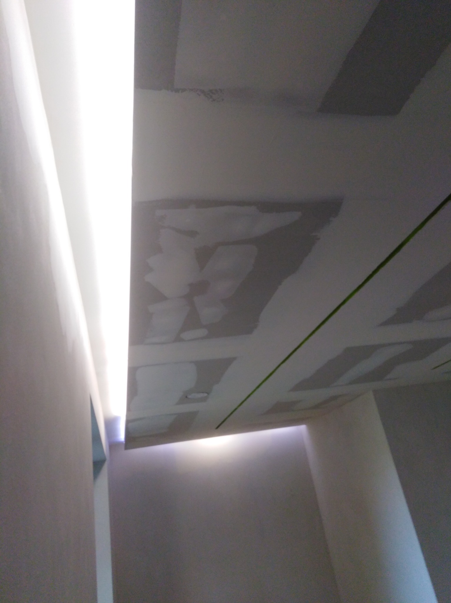 Sufit z płyt kartonowo-gipsowych w trakcie szpachlowania, widoczna zielona linia lasera wyznaczająca poziom, oświetlenie LED wzdłuż krawędzi.