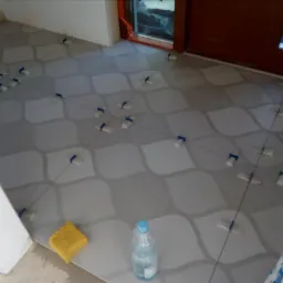 Układanie wzorzystych płytek podłogowych, widoczne krzyżyki dystansowe, gąbka i butelka z wodą.