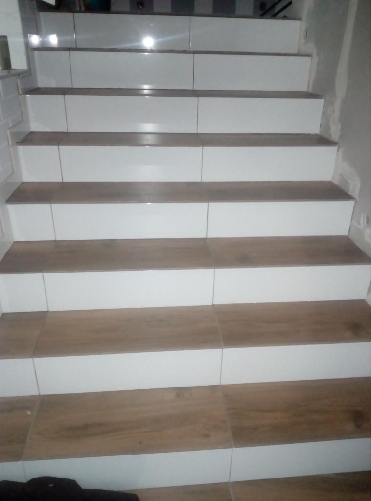 Schody wyłożone płytkami imitującymi drewno z białymi podstopnicami, widok z dołu, częściowo widoczna ściana z białej cegły.