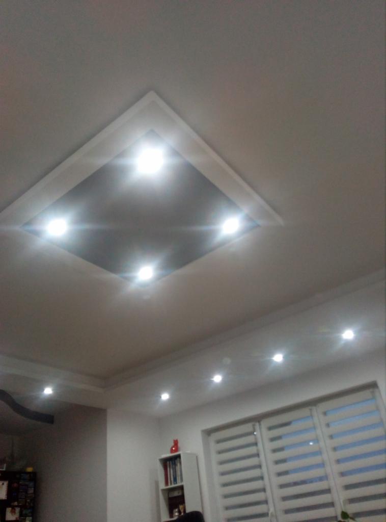 Nowoczesny sufit z wbudowanym oświetleniem punktowym, widok z dołu, białe ściany i rolety w tle.