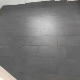 Ułożona podłoga z szarych, podłużnych płytek w łazience, widoczne ślady po fugowaniu przy ścianach.