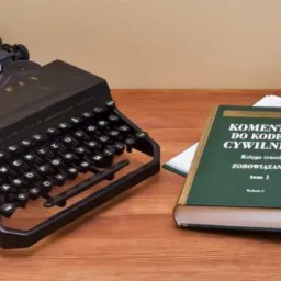 Staromodna maszyna do pisania z dokumentem, obok otwarty komentarz do kodeksu cywilnego na drewnianym biurku.