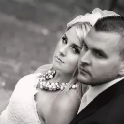 Czarno-białe ujęcie młodej pary: panna młoda z blond włosami i wyrazistym makijażem oraz pan młody w ciemnym garniturze, oboje spoglądają w bok z powagą.