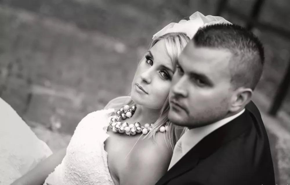 Czarno-białe ujęcie młodej pary: panna młoda z blond włosami i wyrazistym makijażem oraz pan młody w ciemnym garniturze, oboje spoglądają w bok z powagą.