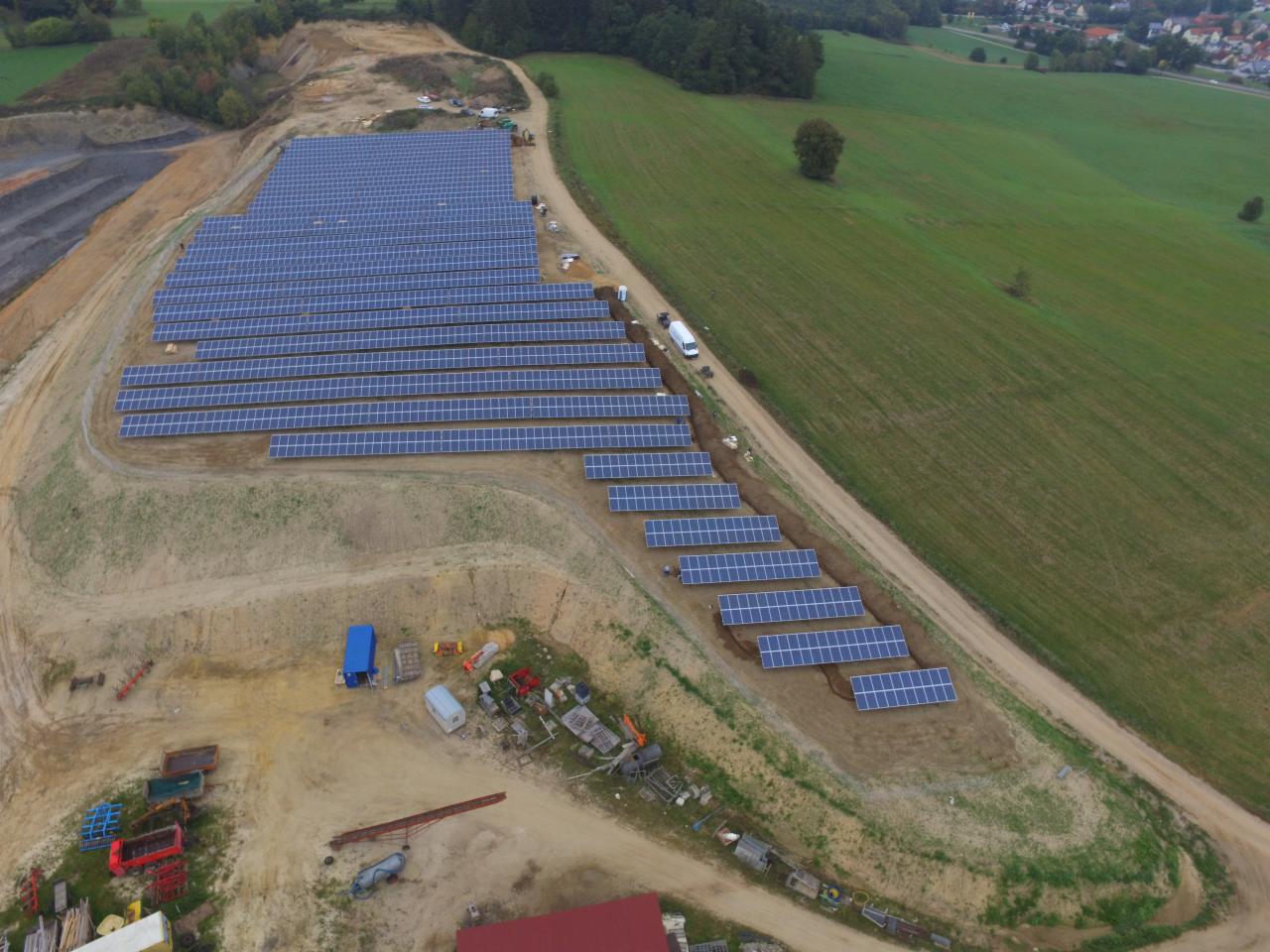 Widok z lotu ptaka na rozległą instalację paneli słonecznych na zboczu wzgórza, z widocznymi maszynami budowlanymi i pojazdem dostawczym w pobliżu.