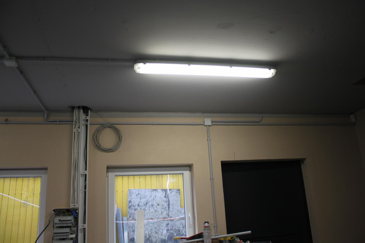 Wnętrze z widoczną instalacją elektryczną: lampa jarzeniowa pod sufitem, kable w korytkach i rurkach na ścianie, skrzynka elektryczna przy oknie.