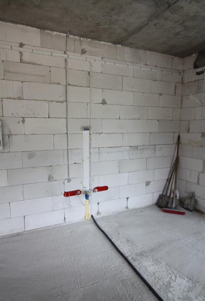 Wewnętrzna instalacja elektryczna w surowym pomieszczeniu z betonową podłogą i ścianami z białych bloczków, widoczne kable w listwach, puszki elektryczne oraz fragment instalacji wodnej...