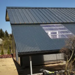 Nowoczesna hala z szarej blachy trapezowej z doświetleniem z paneli poliwęglanowych, widok z zewnątrz w słoneczny dzień.