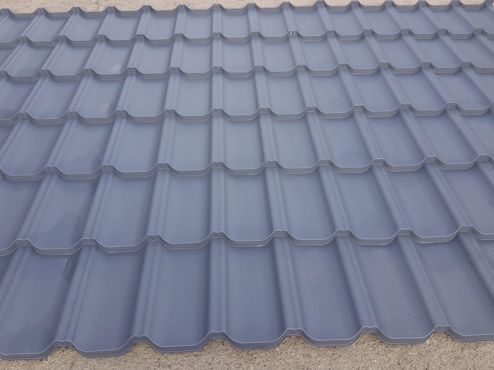 Szare metalowe dachówki modułowe w regularnym wzorze, widoczne z bliska, z delikatnym cieniowaniem podkreślającym kształt.