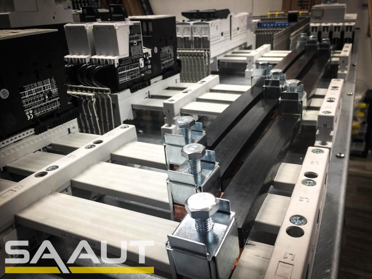 Szyna prądowa zamocowana za pomocą metalowych uchwytów z nakrętkami, widoczne moduły i elementy instalacji elektrycznej na szynach DIN.