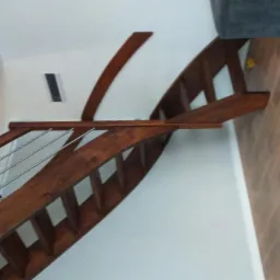 Zakrzywione schody drewniane z metalowymi balustradami, widok z dołu, brązowe drewno, białe ściany, parkiet ułożony w jodełkę.