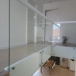 Szklana balustrada z białymi elementami mocującymi, widok z góry na stół i krzesła w jasnym wnętrzu domu.