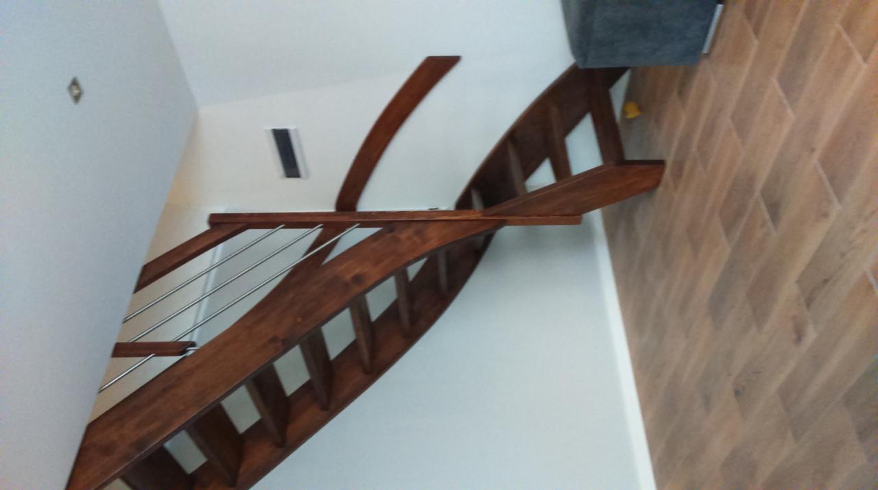 Zakrzywione schody drewniane z metalowymi balustradami, widok z dołu, brązowe drewno, białe ściany, parkiet ułożony w jodełkę.
