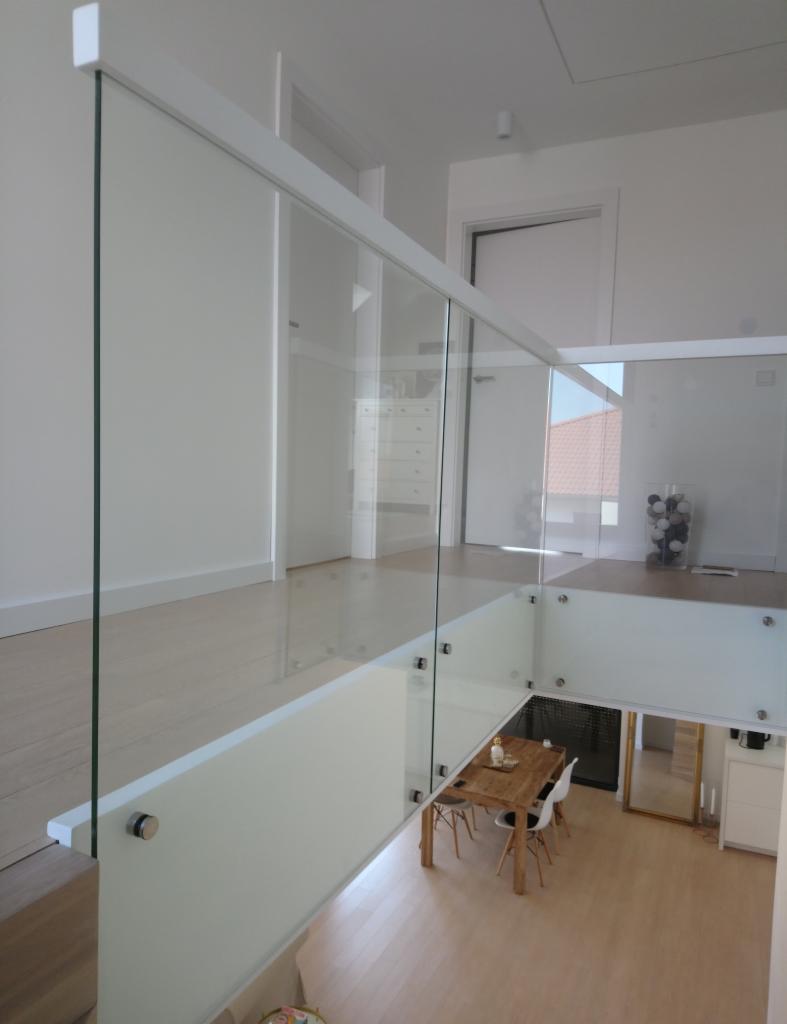 Szklana balustrada z białymi elementami mocującymi, widok z góry na stół i krzesła w jasnym wnętrzu domu.