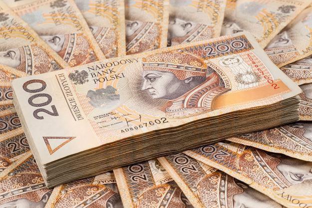 Stos banknotów dwustuzłotowych na tle rozłożonych banknotów, widoczny portret króla Zygmunta I Starego.