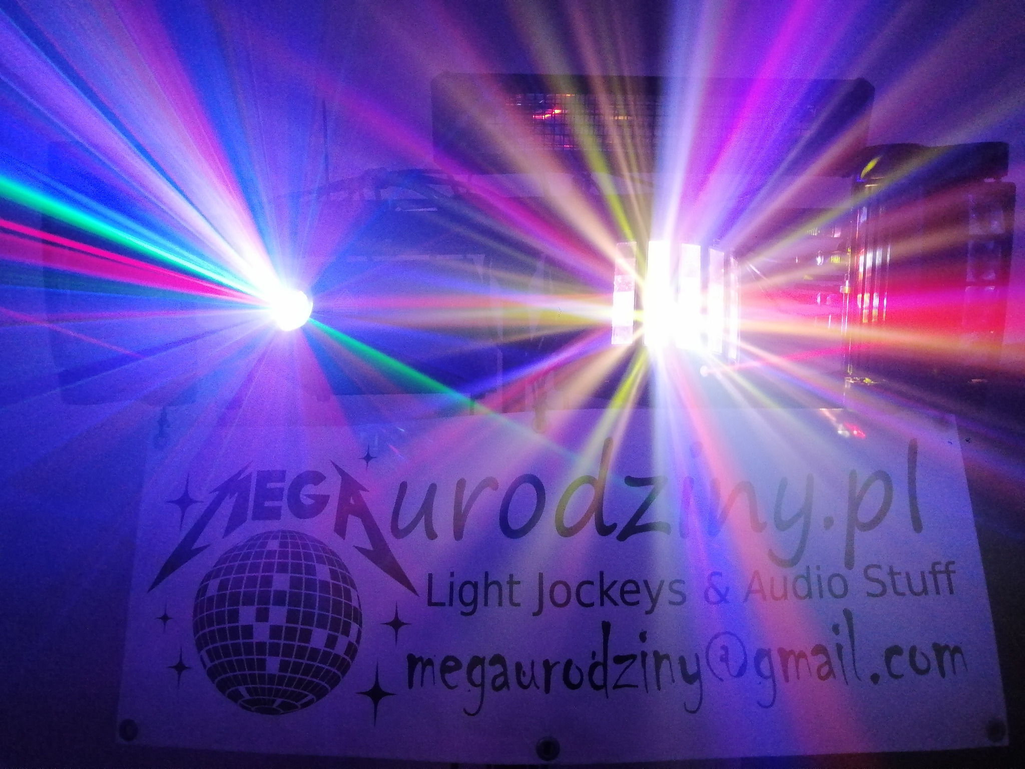 Wiązki kolorowych świateł laserowych oświetlają baner reklamowy z napisem 'MEGAurodziny.pl Light Jockeys & Audio Stuff' i grafiką kuli dyskotekowej.