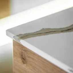 Biały blat z konglomeratu z delikatnym, beżowym żyłkowaniem, zamontowany na szafce z jasnego drewna z wyraźnym usłojeniem i sękiem.