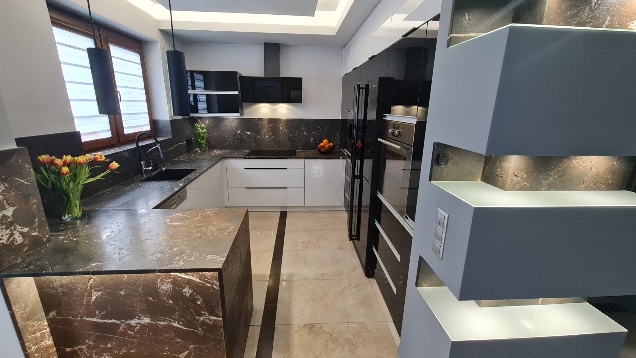Nowoczesna kuchnia z marmurowym blatem, czarnym zlewem i bukietem tulipanów w wazonie, oświetlona wiszącymi lampami i podświetleniem szafek.