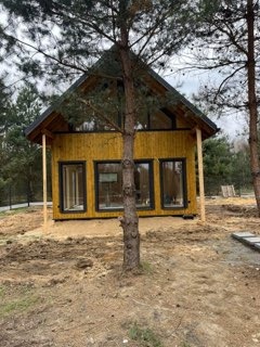 Nowo wybudowany, drewniany domek letniskowy w Radomsku, z dużymi oknami i jasną elewacją, otoczony piaszczystym terenem przed zagospodarowaniem ogrodu.