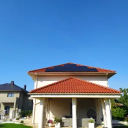 Dom jednorodzinny z panelami słonecznymi na dachu, widok z poziomu gruntu w słoneczny dzień.