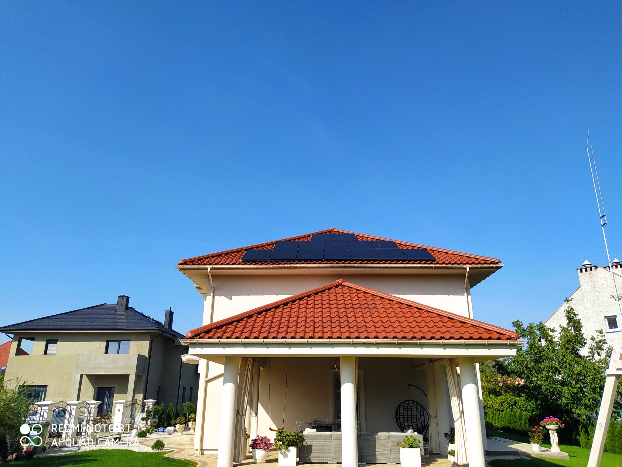 Dom jednorodzinny z panelami słonecznymi na dachu, widok z poziomu gruntu w słoneczny dzień.