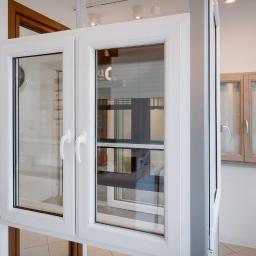 Okna Warszawa - Prezentacja dwuskrzydłowego okna z białymi ramami, widok na inne okna w tle, ekspozycja w salonie.