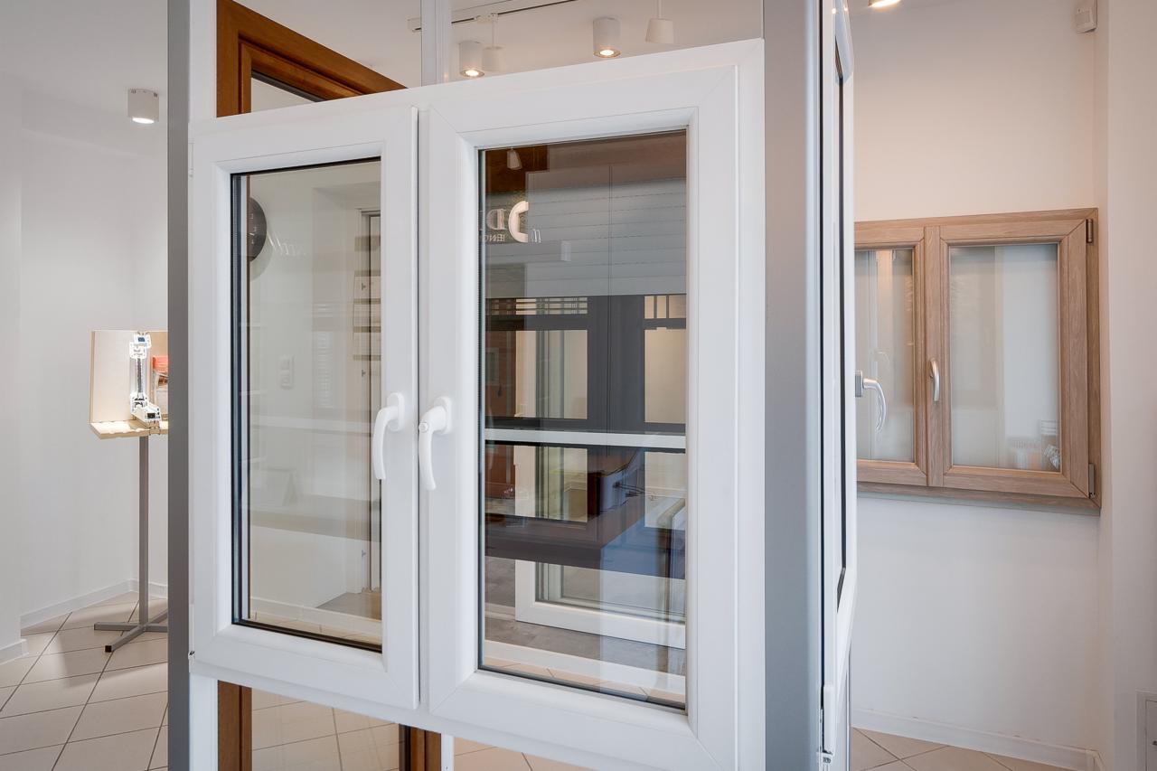 Prezentacja dwuskrzydłowego okna z białymi ramami, widok na inne okna w tle, ekspozycja w salonie.