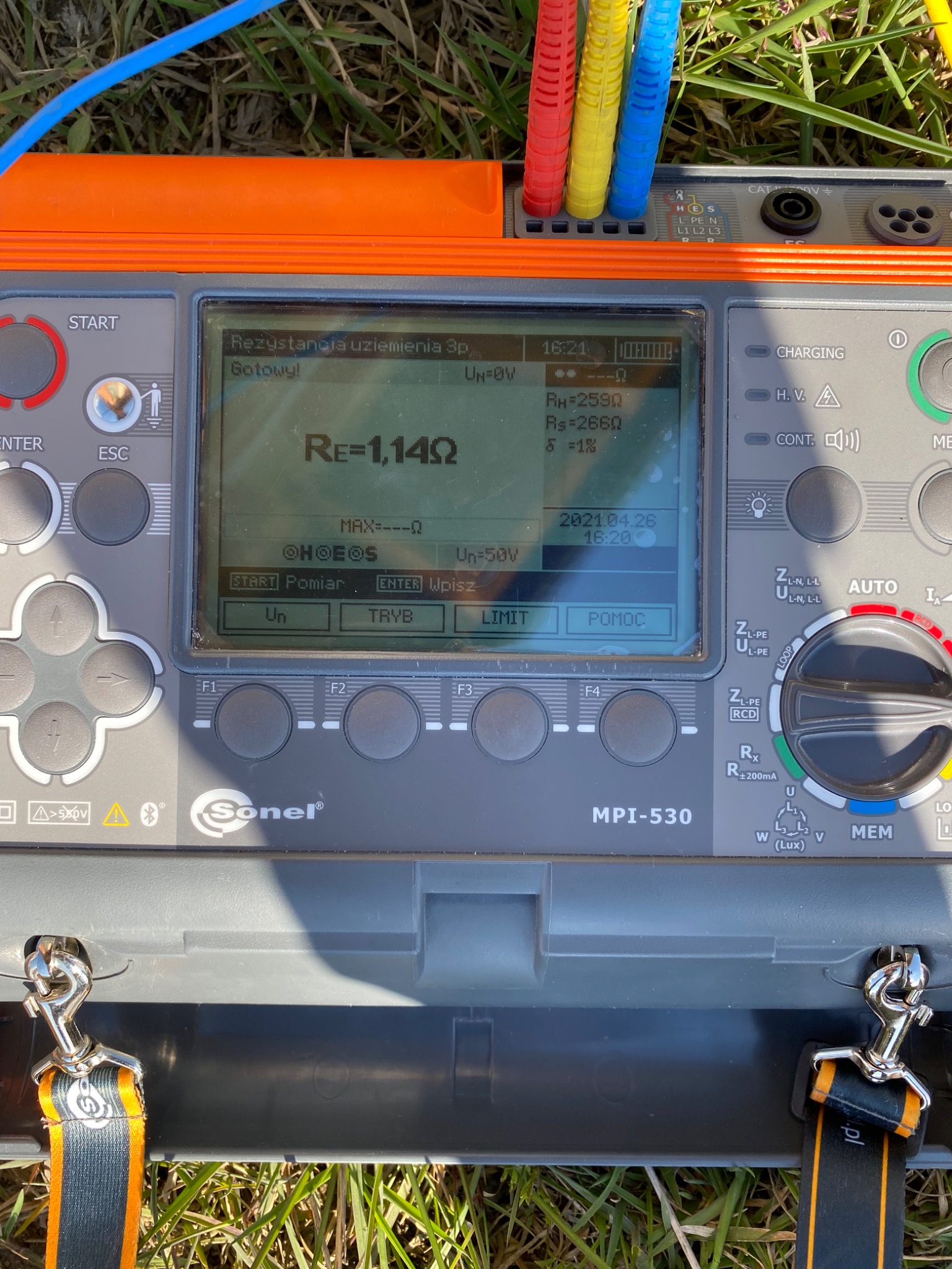 Miernik Sonel MPI-530 na trawie, wyświetlający wynik pomiaru rezystancji uziemienia 1.14Ω, z podłączonymi przewodami pomiarowymi w kolorach czerwonym, żółtym i niebieskim.