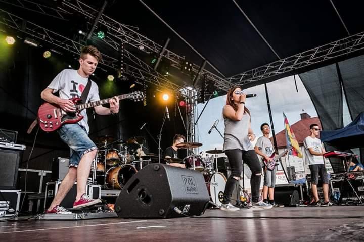 Występujący na scenie zespół: wokalistka z mikrofonem, gitarzysta w koszulce z sercem, perkusista i klawiszowiec, oświetlenie sceniczne, nagłośnienie POL Audio.