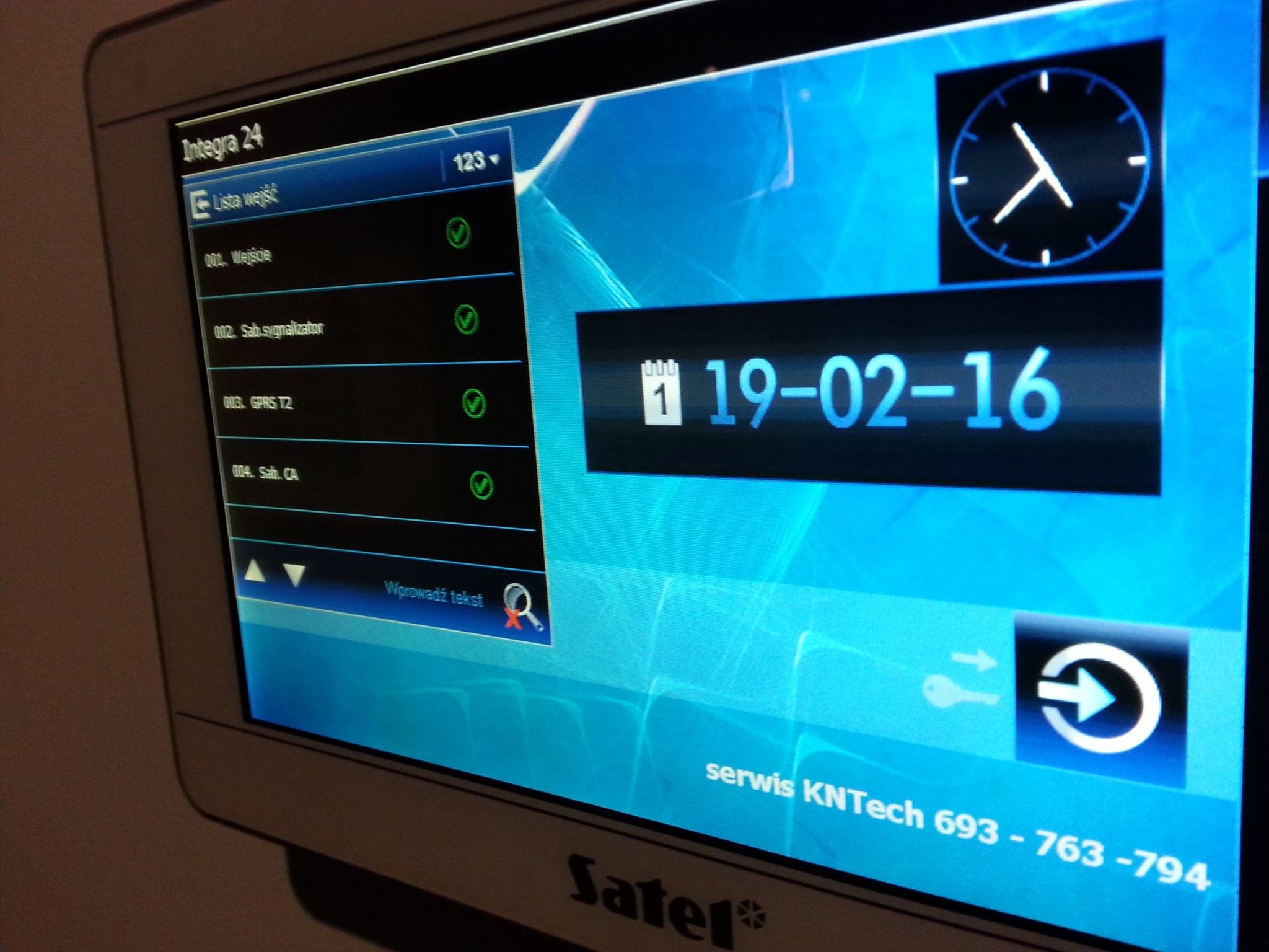 Ekran dotykowy centrali alarmowej Satel Integra 24 z listą wejść, datą 19-02-16 i ikoną zegara, prezentujący status systemu