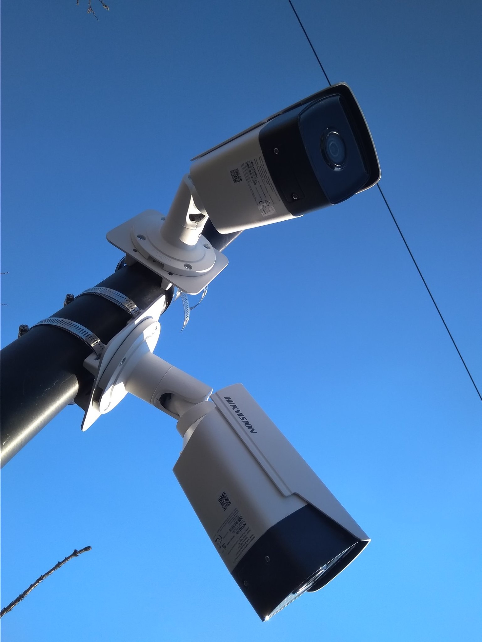 Dwie kamery monitoringu marki Hikvision zamontowane na czarnym słupie, widok z dołu na tle błękitnego nieba.