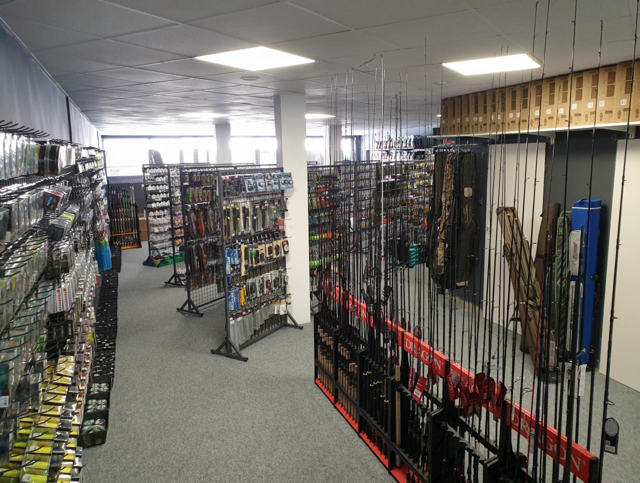 Wnętrze sklepu z szerokim asortymentem wędek, przynęt i akcesoriów wędkarskich, z widocznymi regałami i ekspozytorami.