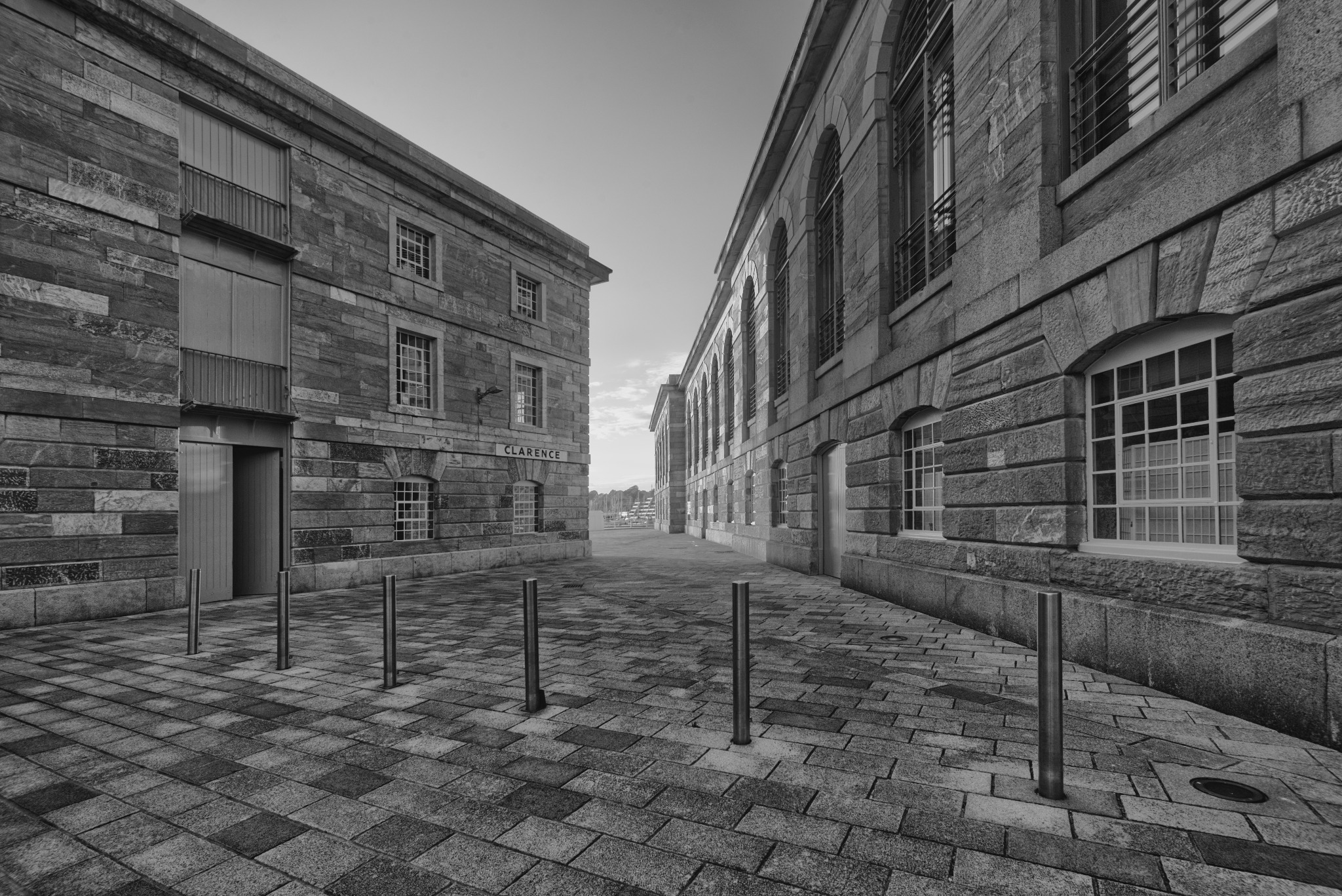 Czarno-białe zdjęcie uliczki między dwoma budynkami z kamienia. Jeden z budynków ma tabliczkę z napisem 'CLARENCE'.