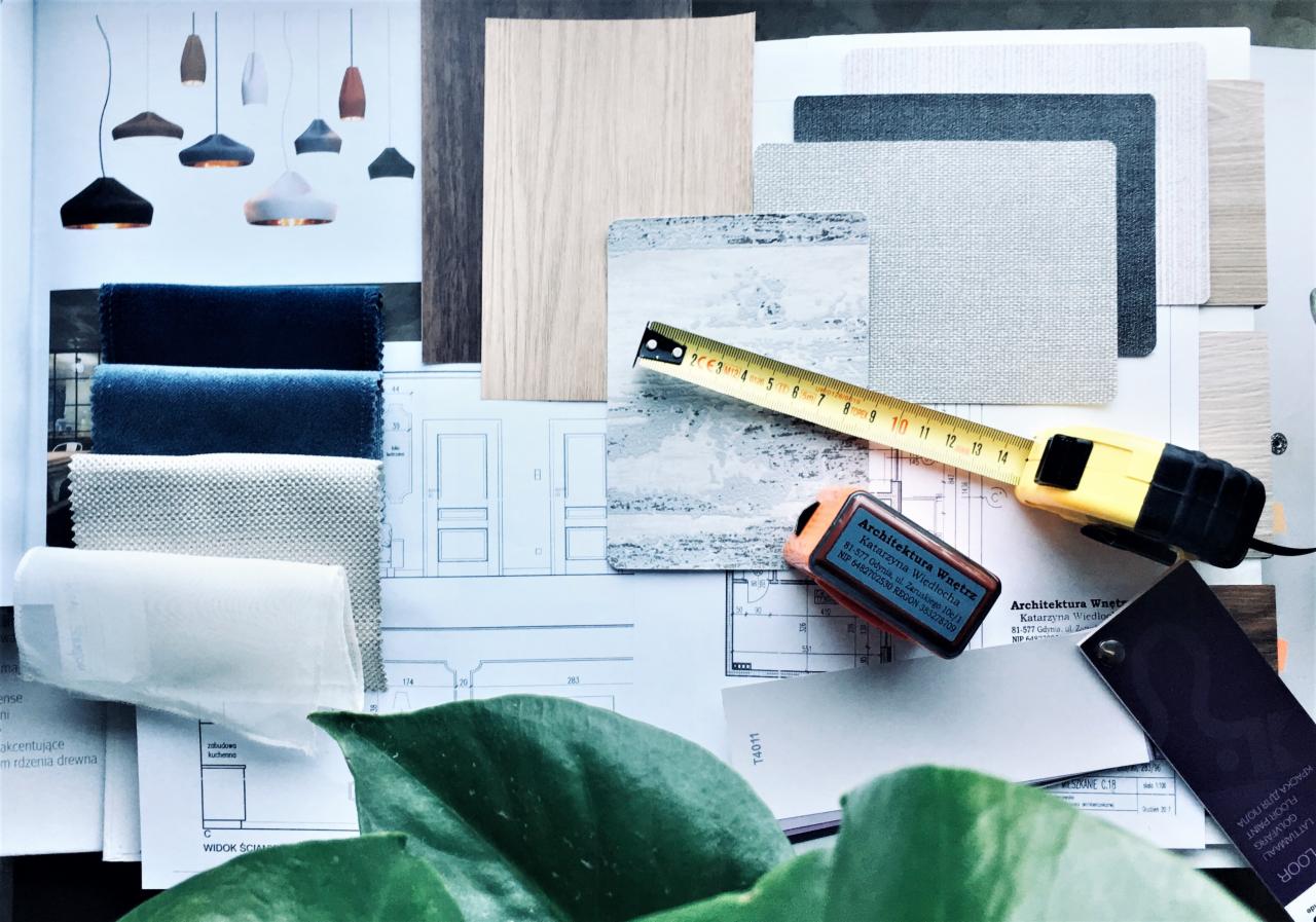 Zestawienie próbek materiałów wykończeniowych: tkaniny welurowe w odcieniach granatu i beżu, panele drewnopodobne, płytki imitujące marmur, próbki farb, żółta miarka zwinięta do 14 cm, wizytówka...