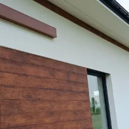 Fragment elewacji domu z drewnopodobną okładziną i oknem, widok z dołu. Elementy dekoracyjne w kolorze brązowym. Nowoczesne wykończenie.