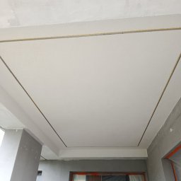 TOP BUD Kamil Sadowski - Wykończony sufit podwieszany z listwami LED w nowym budynku. Świeżo położona gładź szpachlowa na suficie. Widoczne zabezpieczone okna folią malarską.